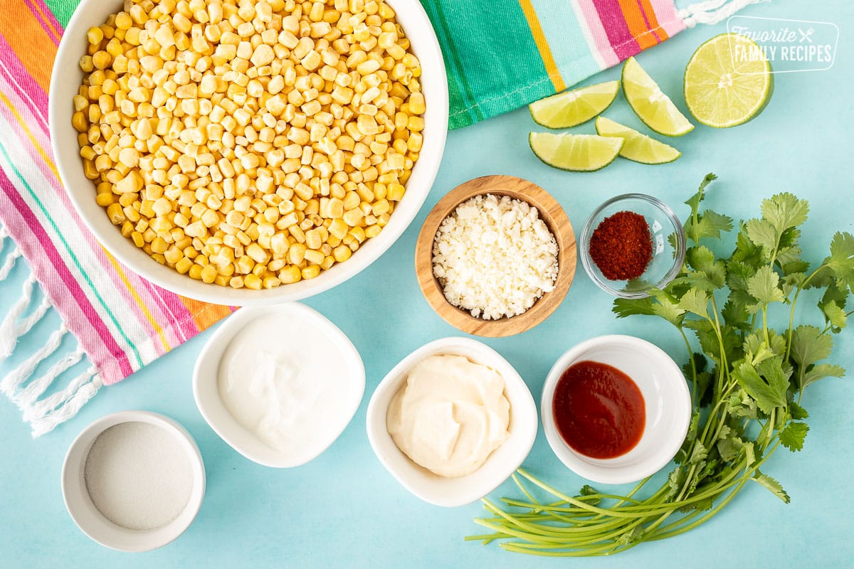 Ingredients to make Elite in a Cup including frozen corn, cotija cheese, lime wedges, cilantro, sriracha, chili powder, salt, mayonnaise, sour cream and sugar.