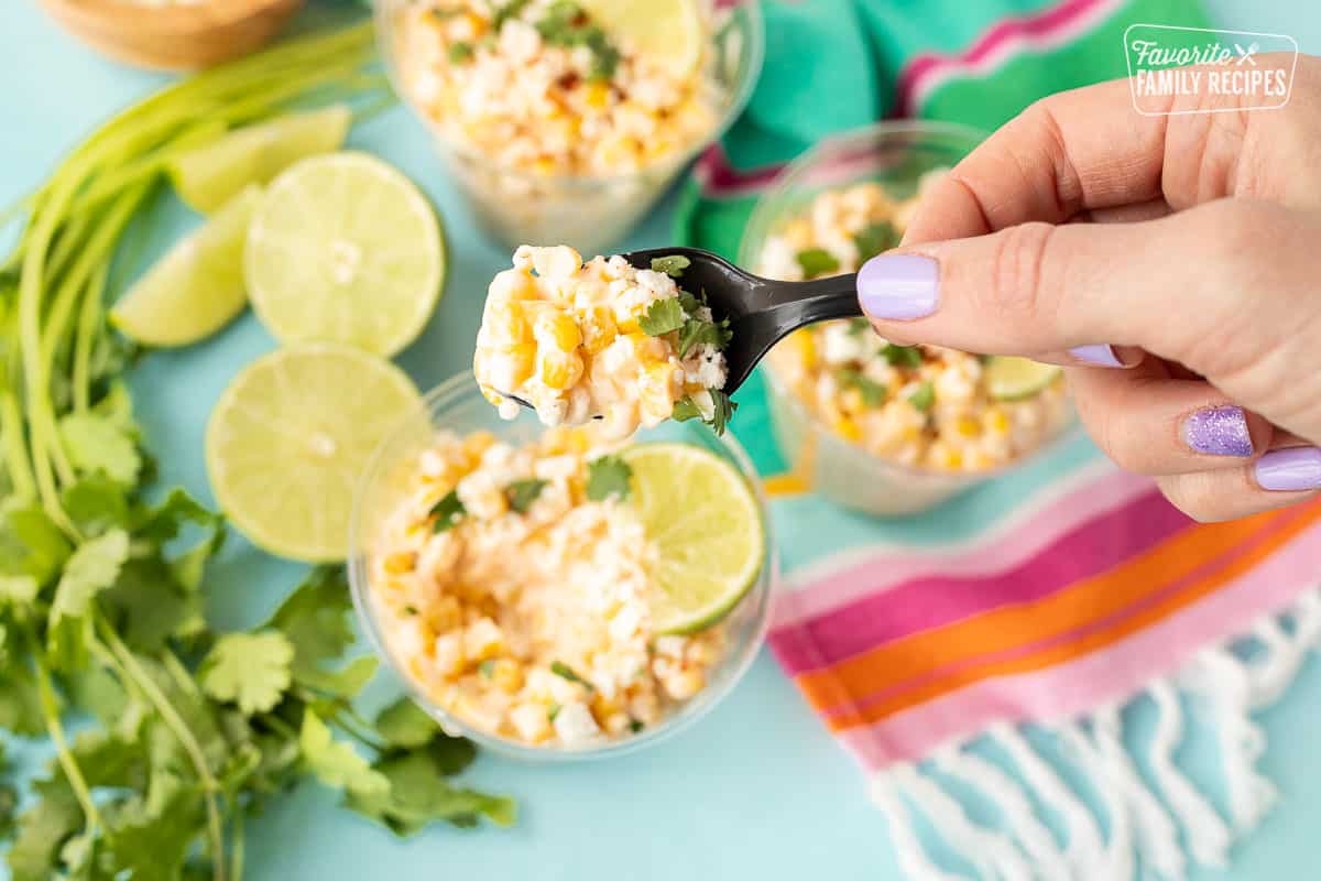 Hand holding a spoon full of Mexican Street Corn from a cup.