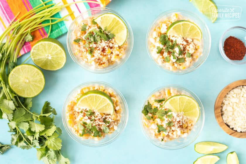 Four cups with Mexican Street Corn garnished with lime, cilantro and chili powder.