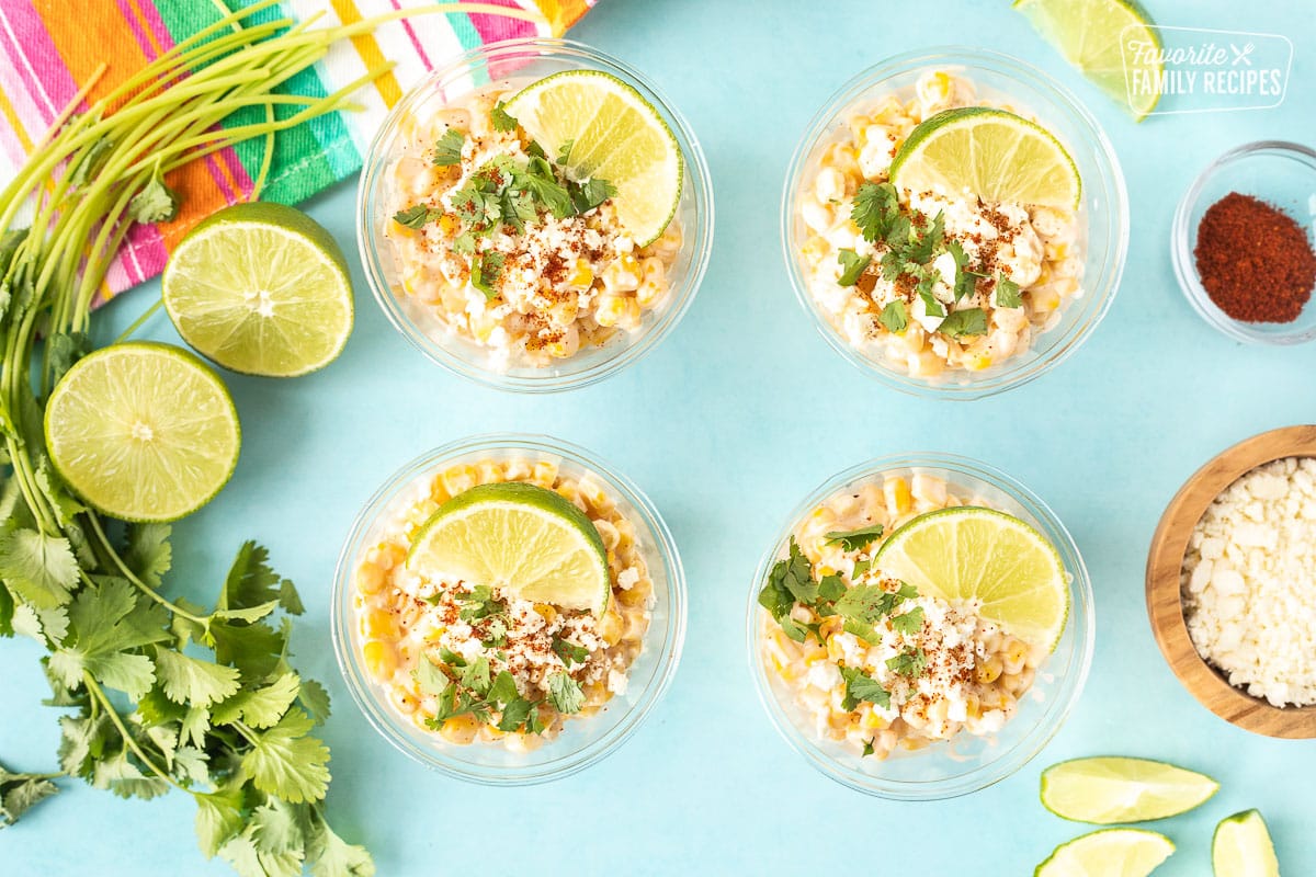 Four cups with Mexican Street Corn garnished with lime, cilantro and chili powder.