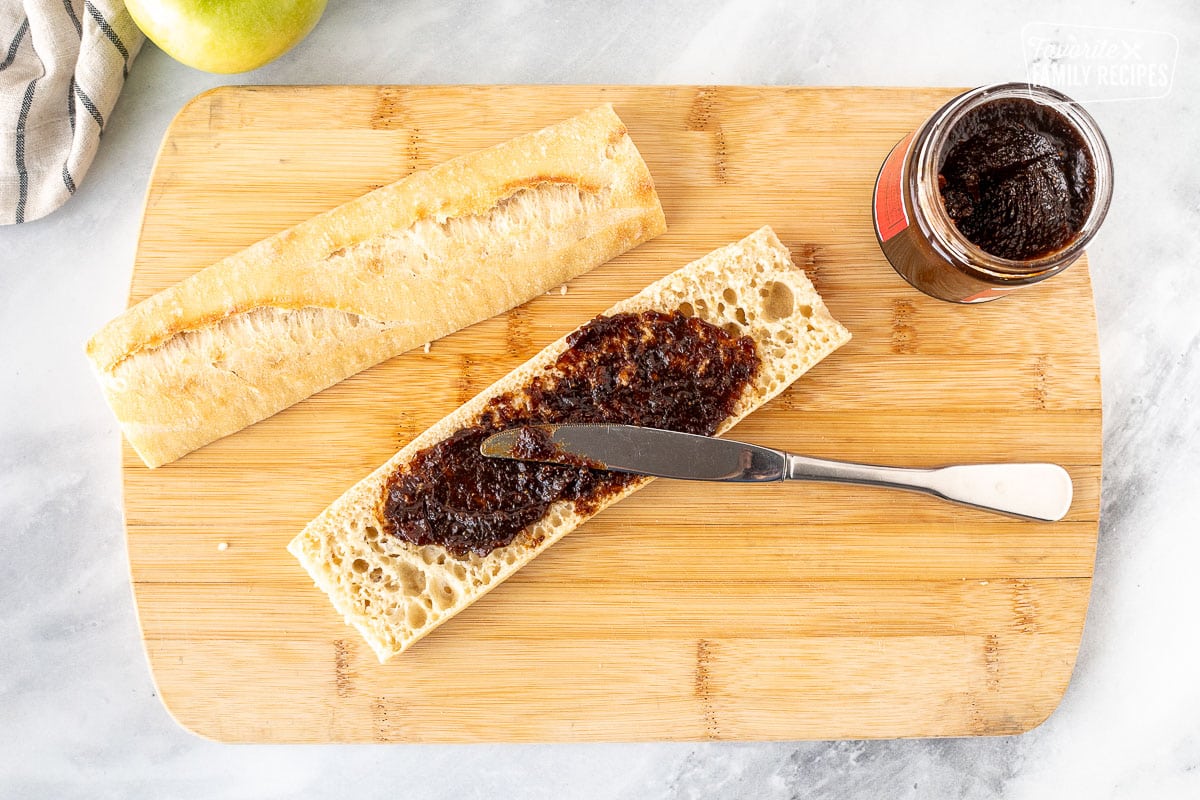 Spreading Fig butter on bottom half of the bread with a butter knife on a cutting board.