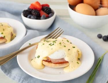 two plates of eggs benedict with a bowl of berries and a bowl of eggs in the background