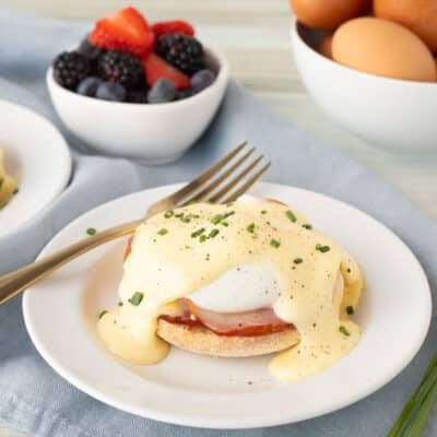 two plates of eggs benedict with a bowl of berries and a bowl of eggs in the background