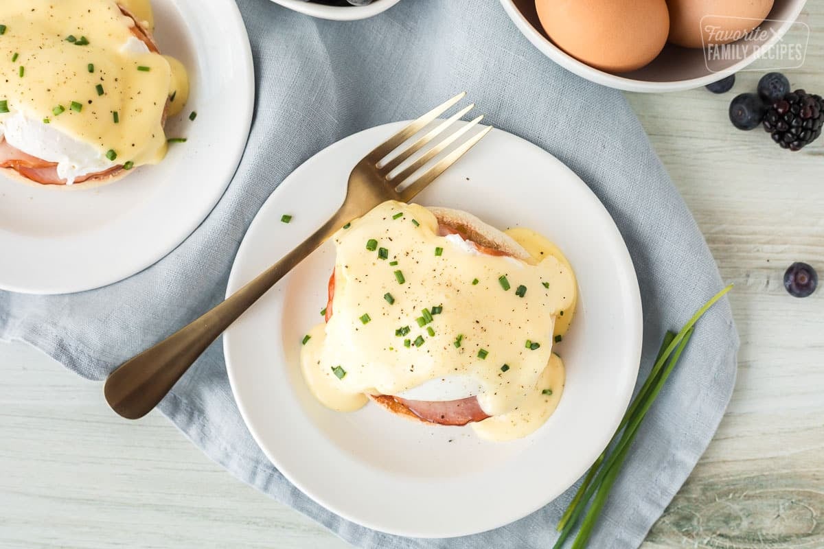 two plates of eggs benedict with a bowl of eggs in the background