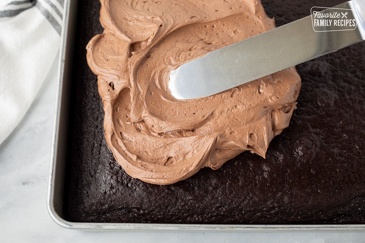 Spreading chocolate buttercream frosting on top of a chocolate cake.