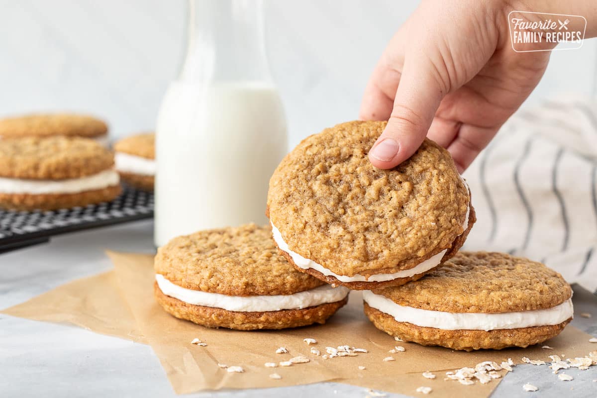 Hand grabbing an Oatmeal Cream Pie that is stacked on top of two other Oatmeal Cream Pies.