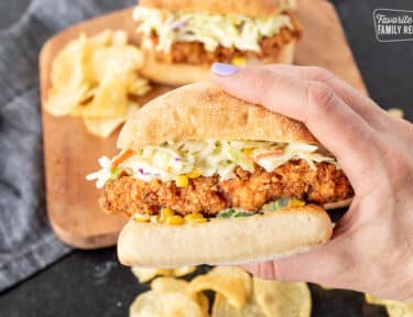 Holding a large Southern Fried Chicken Sandwich with coleslaw and corn sauce.