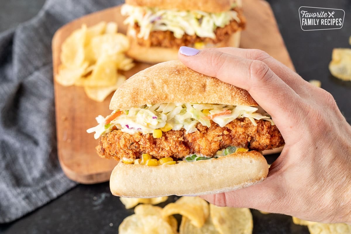 Holding a large Southern Fried Chicken Sandwich with coleslaw and corn sauce.