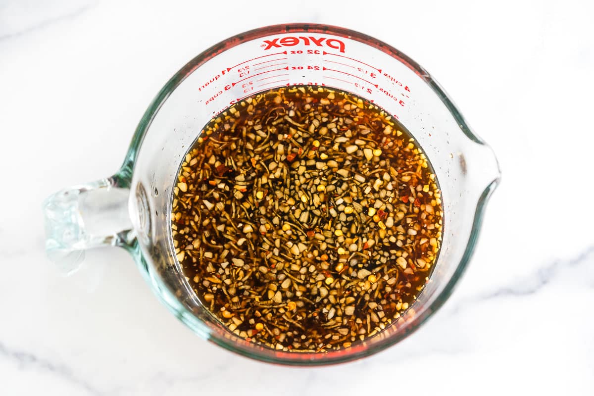 Dark brown sauce with garlic, ginger, and red pepper flakes in a glass measuring cup