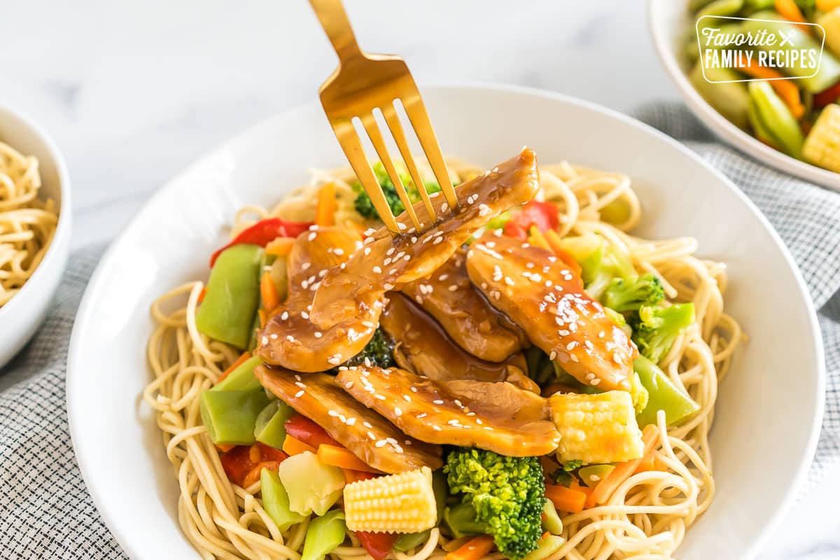 A bowl of honey sesame chicken with a fork taking out a piece of chicken.
