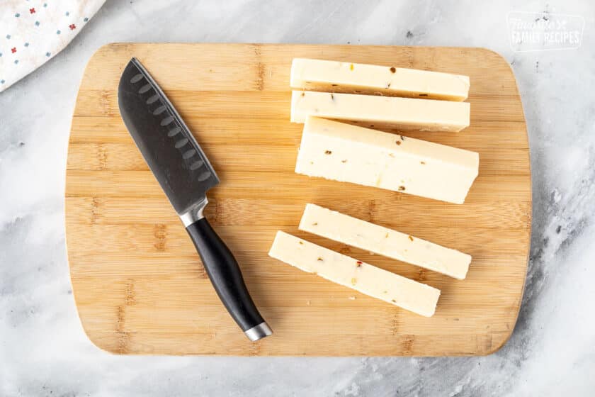 Cutting board with Pepper Jack cheese cut into long sticks. Knife on the side.