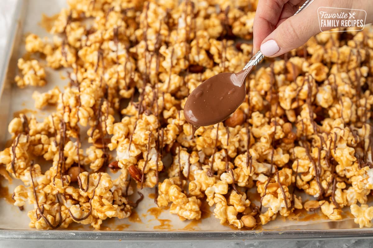 Drizzling melted chocolate on caramel popcorn and nuts.