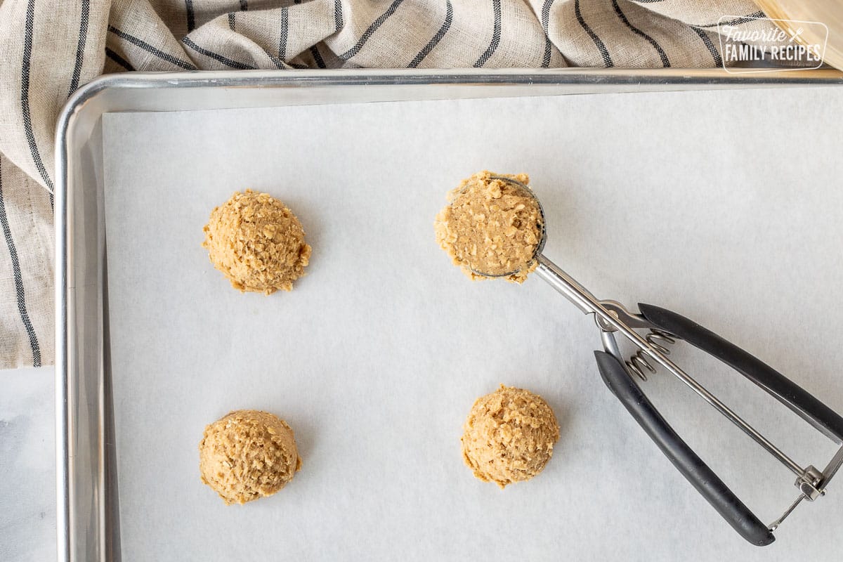 Cookie sheet with parchment paper and oatmeal cookie scoops.
