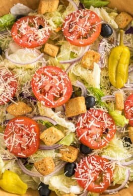 A large bowl with iceberg lettuce, olives, tomatoes, red onions, croutons, pepperoncinis, and parmesan