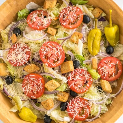 A large bowl with iceberg lettuce, olives, tomatoes, red onions, croutons, pepperoncinis, and parmesan