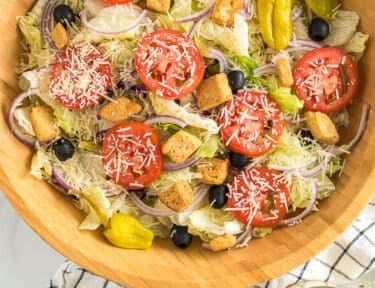 A large bowl of Olive Garden Salad with iceberg lettuce, olives, tomatoes, red onions, croutons, pepperoncinis, and parmesan