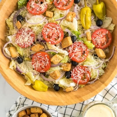 A large bowl of Olive Garden Salad with iceberg lettuce, olives, tomatoes, red onions, croutons, pepperoncinis, and parmesan