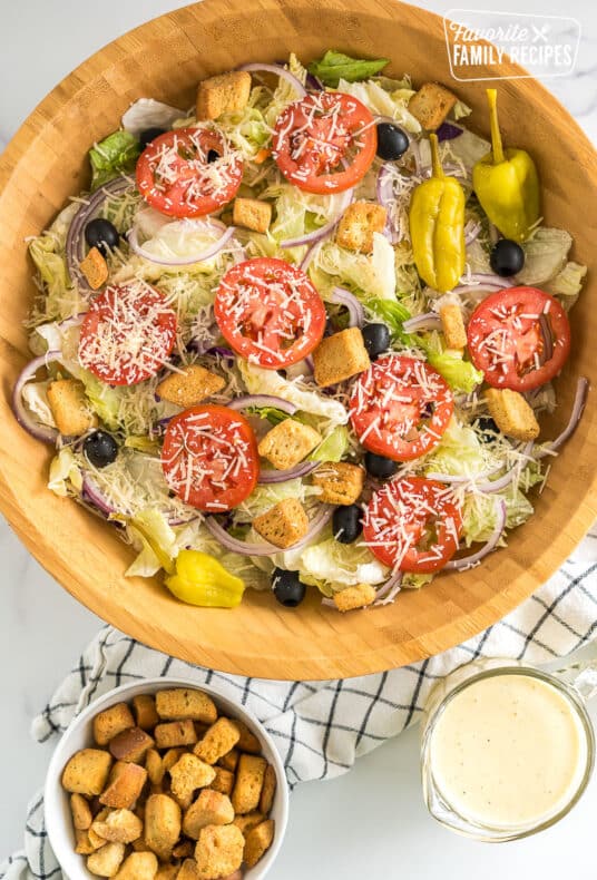 A large bowl of Olive Garden Salad with iceberg lettuce, olives, tomatoes, red onions, croutons, pepperoncinis, and parmesan