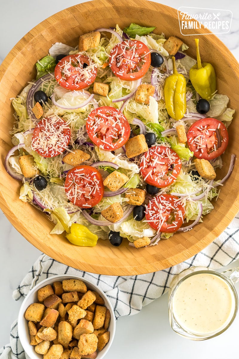 A large bowl of Olive Garden Salad with iceberg lettuce, olives, tomatoes, red onions, croutons, pepperoncinis, and parmesan