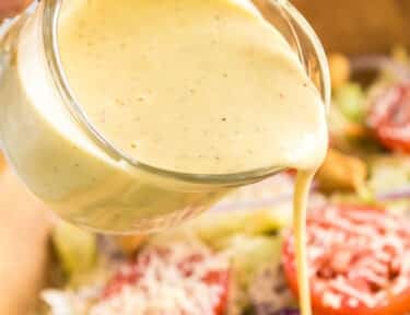 Pouring Olive Garden Salad Dressing over a large bowl of salad