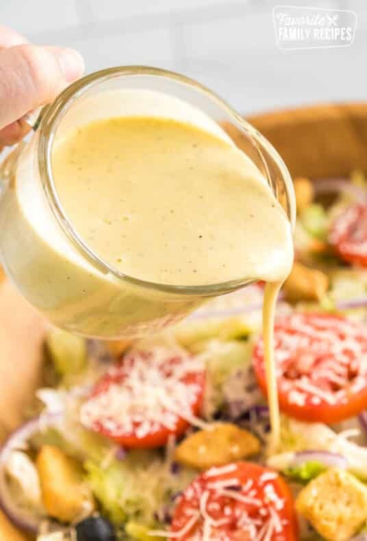 Pouring Olive Garden Salad Dressing over a large bowl of salad