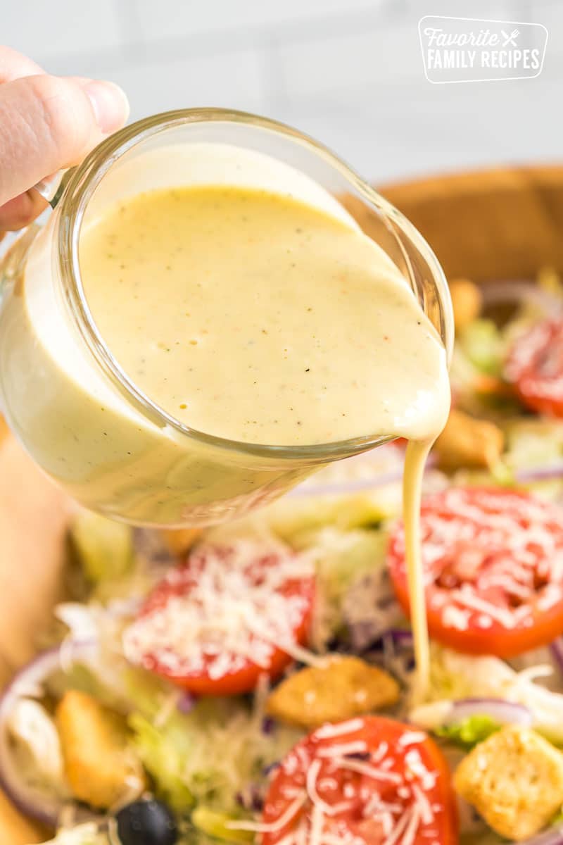 Pouring Olive Garden Salad Dressing over a large bowl of salad.