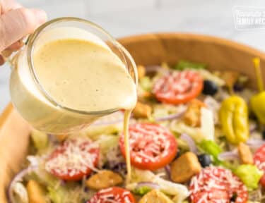 Pouring Olive Garden Salad Dressing over a large bowl of salad
