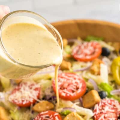 Pouring Olive Garden Salad Dressing over a large bowl of salad