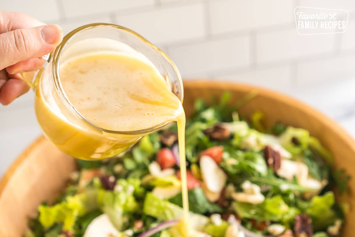 Yellow dressing being poured over a large salad