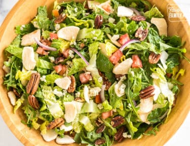 A large bowl with romaine, arugula, tomatoes, freeze-dried fruit, red onions, gorgonzola, and pecans
