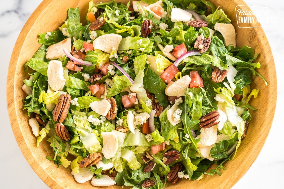 A large bowl with romaine, arugula, tomatoes, freeze-dried fruit, red onions, gorgonzola, and pecans