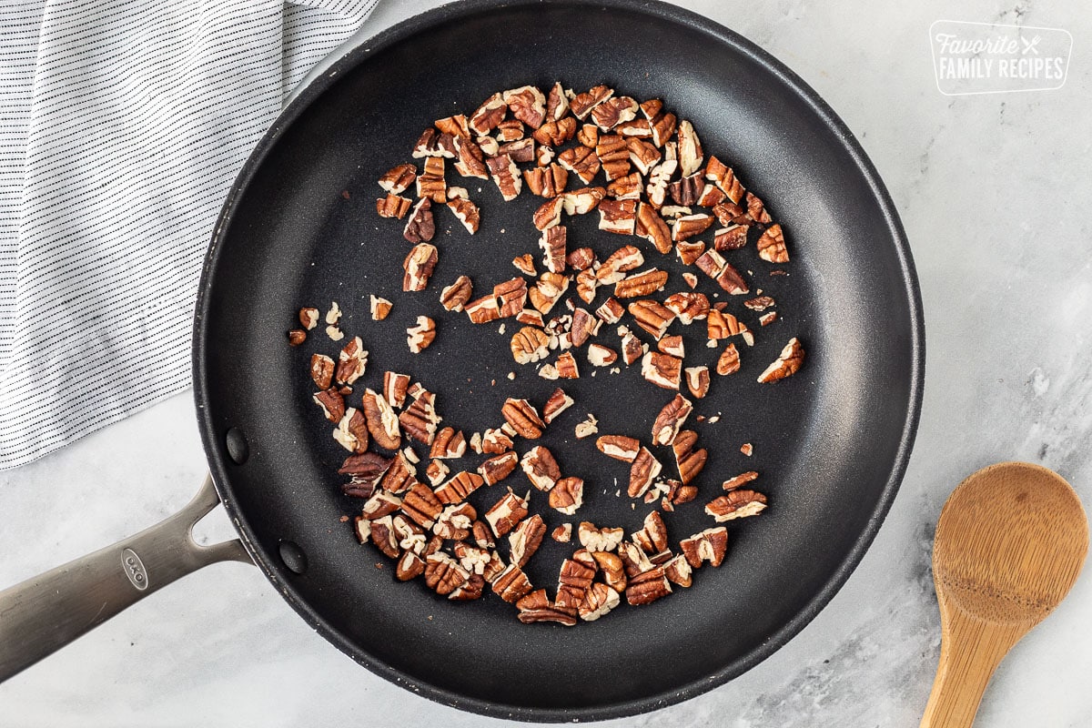 Skillet of pecans with a wooden spoon.