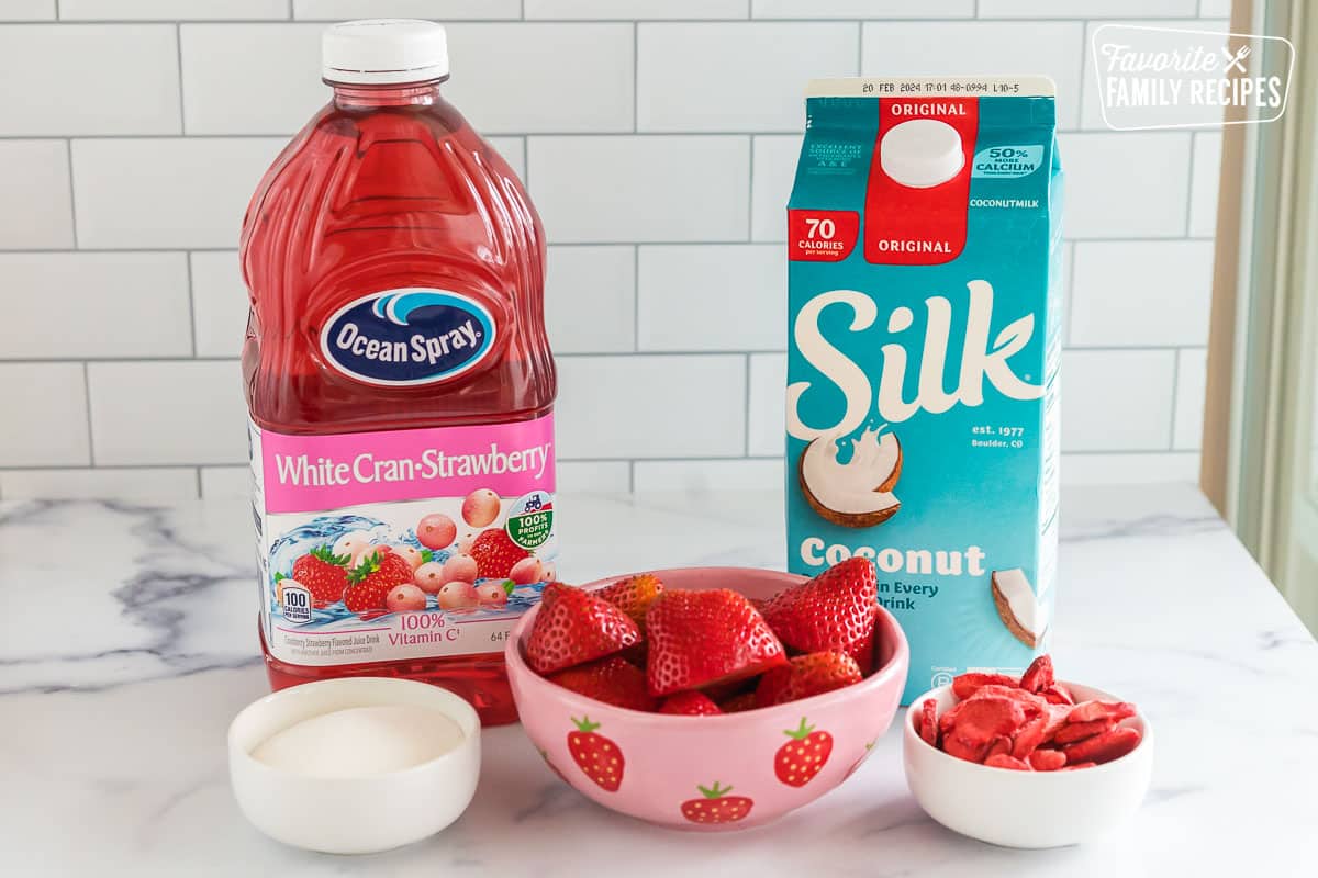 Juice, strawberries, coconut milk, sugar, and freeze dried strawberries on a countertop