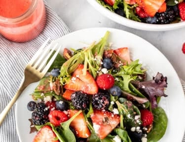 Plate of Nuts About Berries Salad with a fork and extra dressing on the side.