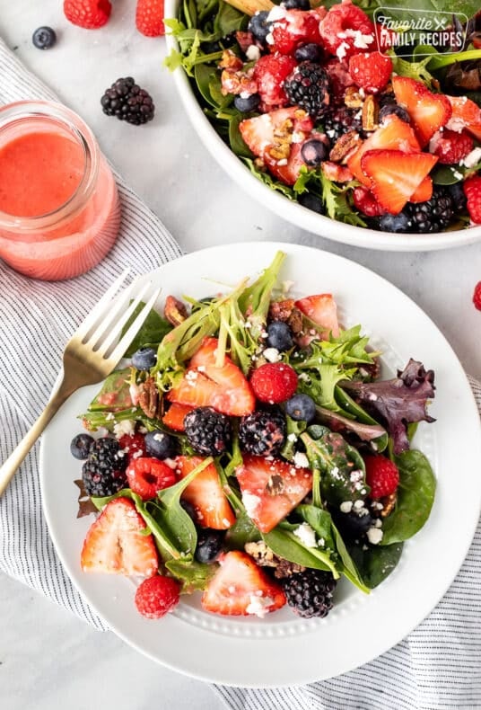 Plate of Nuts About Berries Salad with a fork and extra dressing on the side.