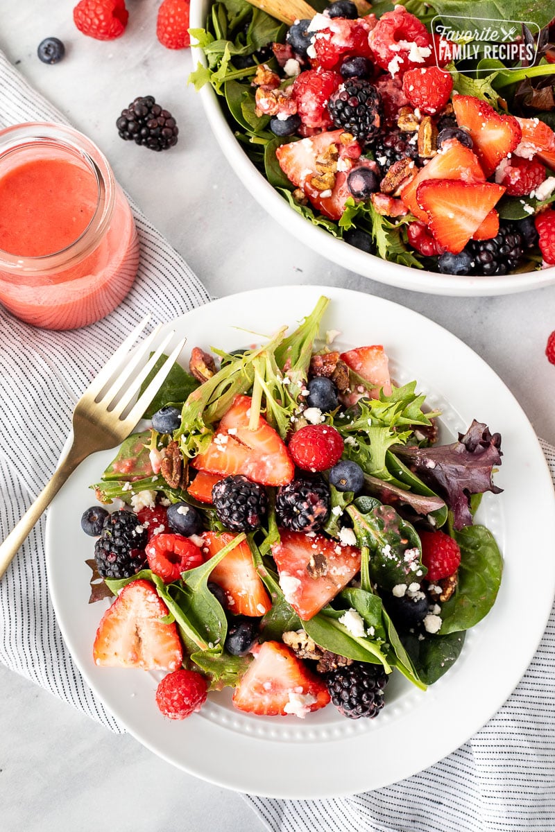 Plate of Nuts About Berries Salad with a fork and extra dressing on the side.