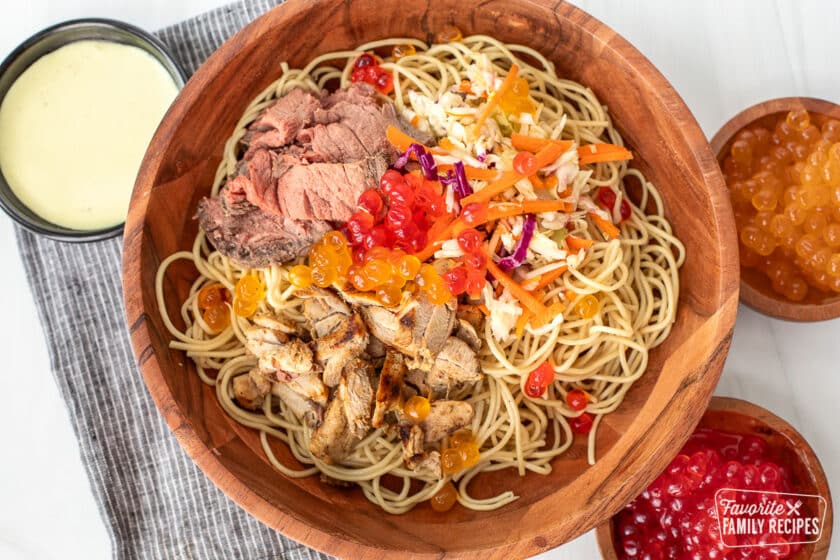 A Satu'li bowl made with noodles, slaw, chicken, beef, and boba balls with a cup of dressing on the side