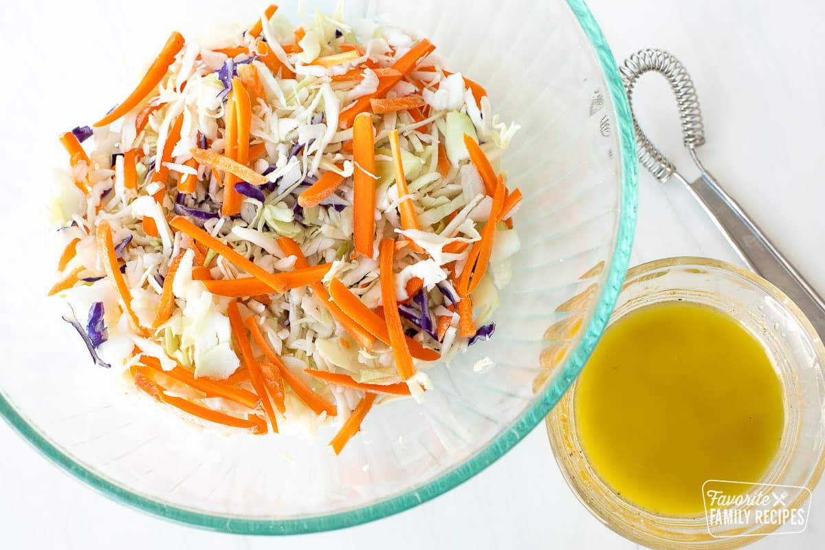 Coleslaw in a glass bowl next to small glass bowl of coleslaw dressing