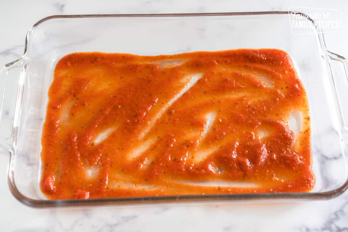 tomato sauce spread on the bottom of a glass baking dish