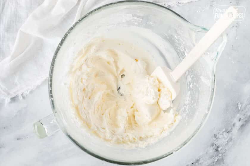Mixing bowl with Vanilla Buttercream Frosting and spatula scraping sides of the bowl.