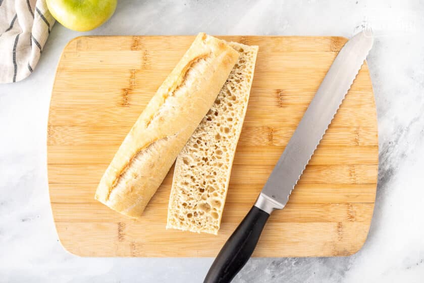 Slicing bread in half on a cutting board with a bread knife.