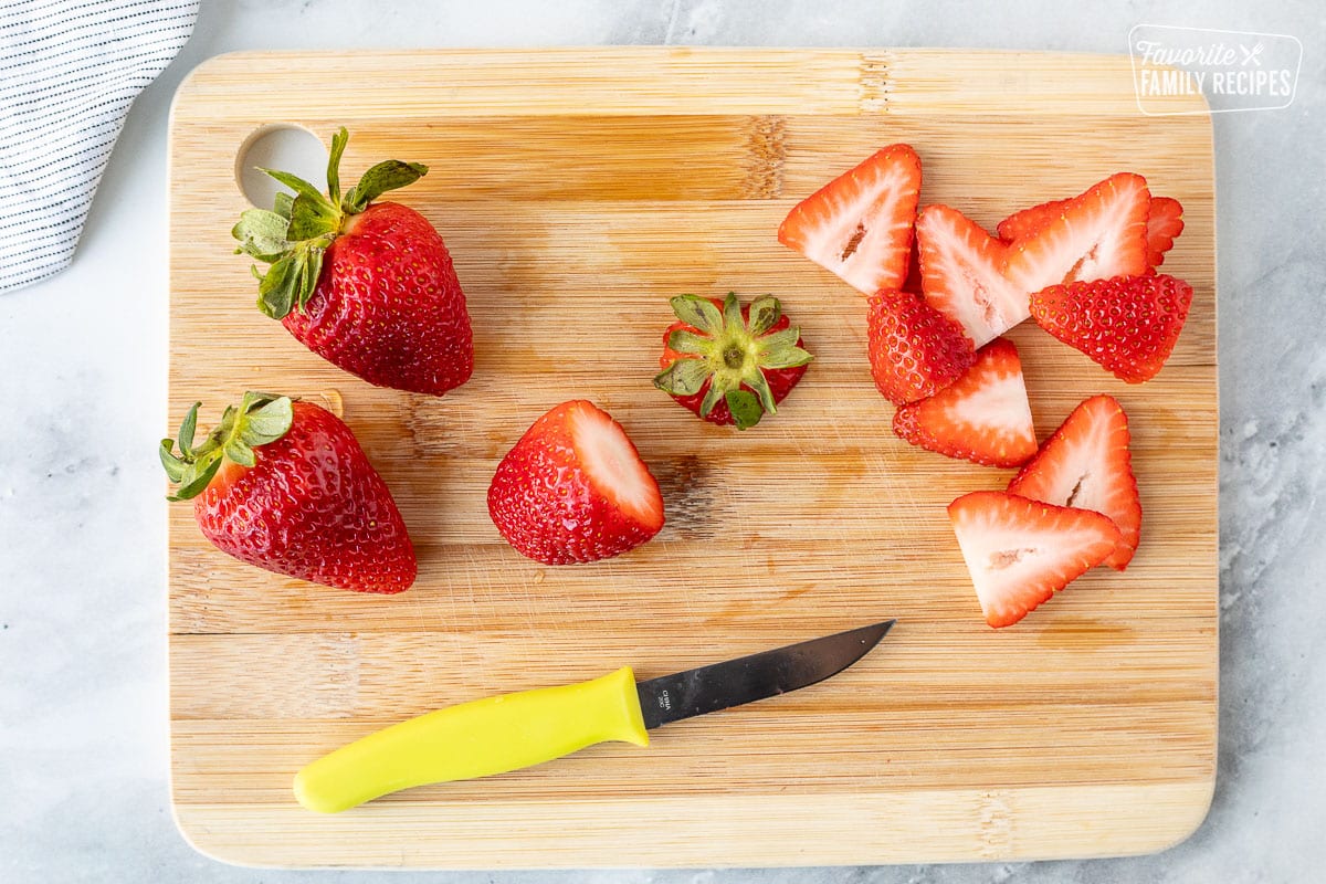Cutting board with sliced strawberries and a knife.
