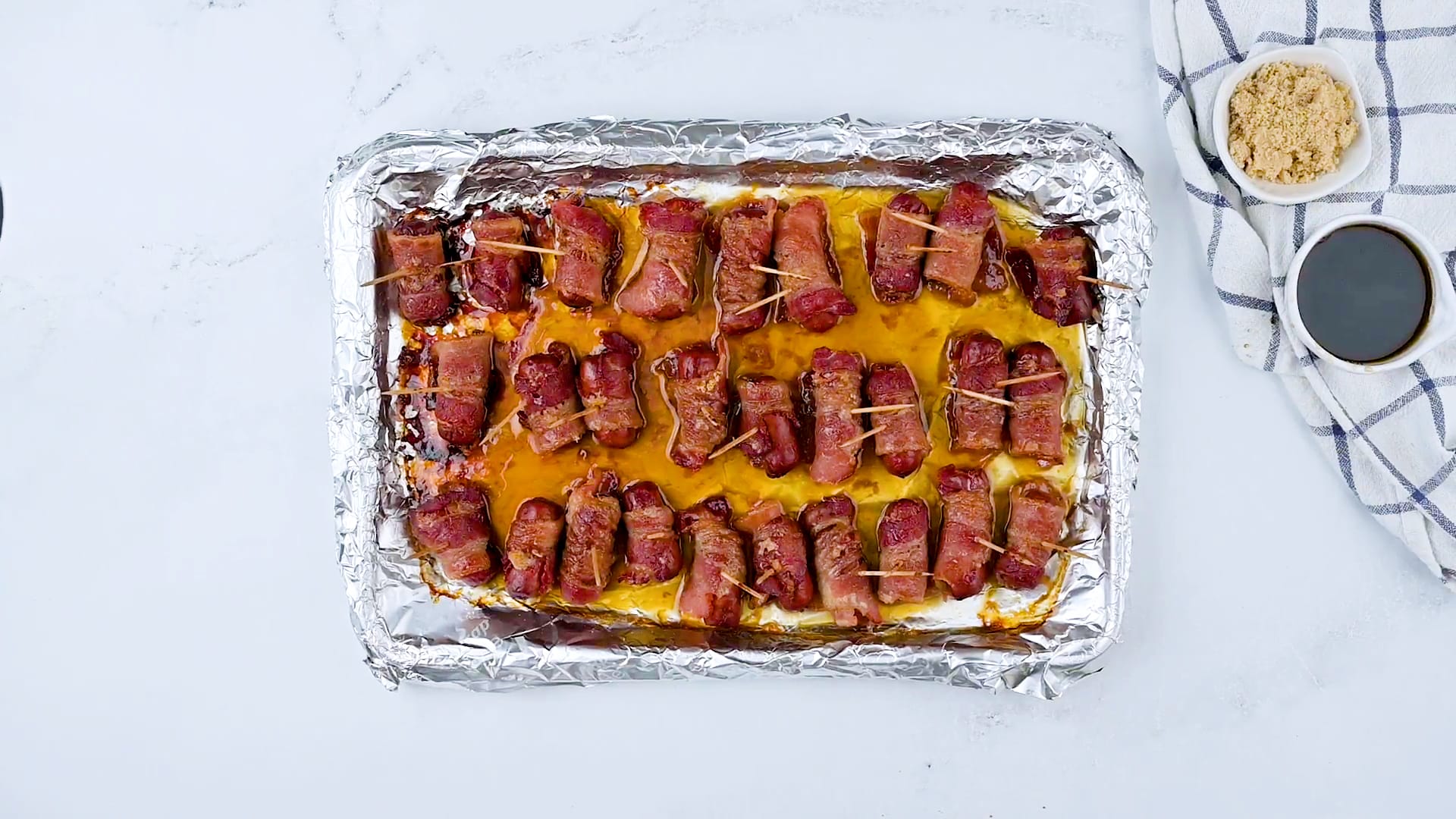 Baked wrapped smokies on a baking sheet with aluminum foil.