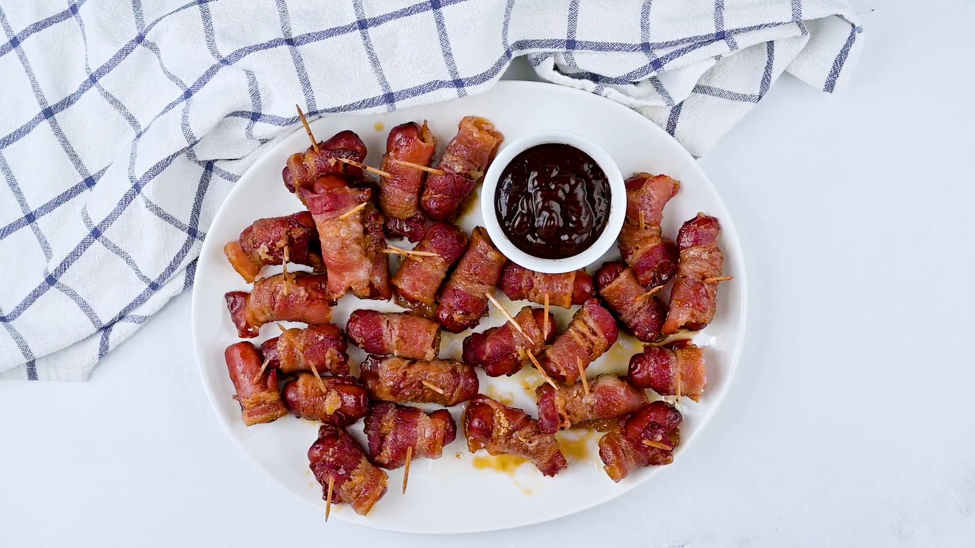 Smokies on a white plate with a toothpick in each one with sauce on the side.