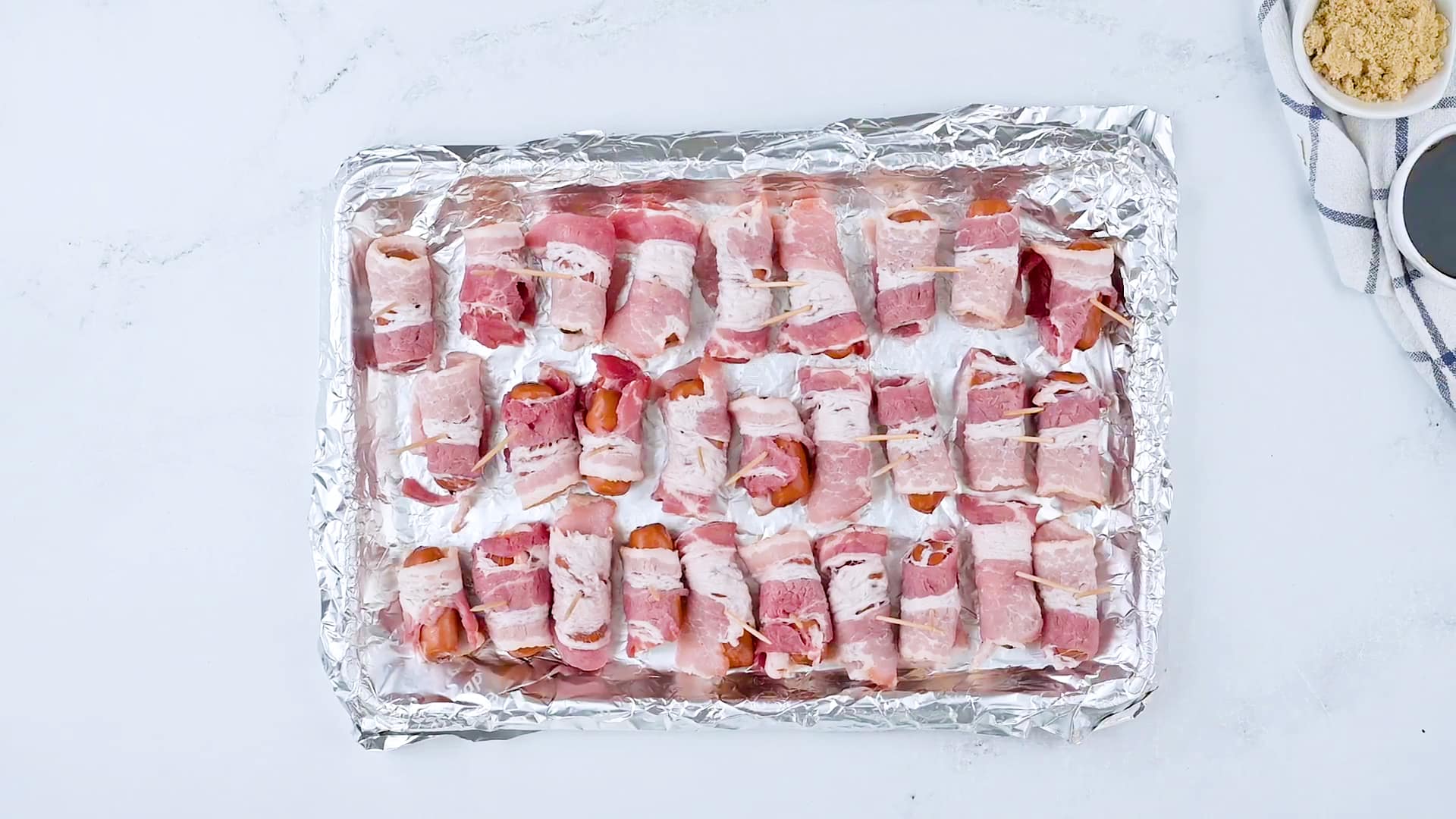 Unbaked smokies wrapped in bacon on a baking sheet with aluminum foil.