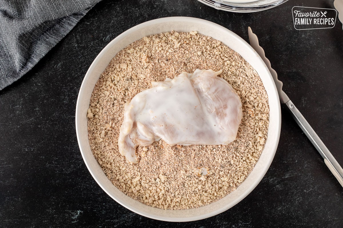 Coated chicken in a bowl of seasoned crumbs.