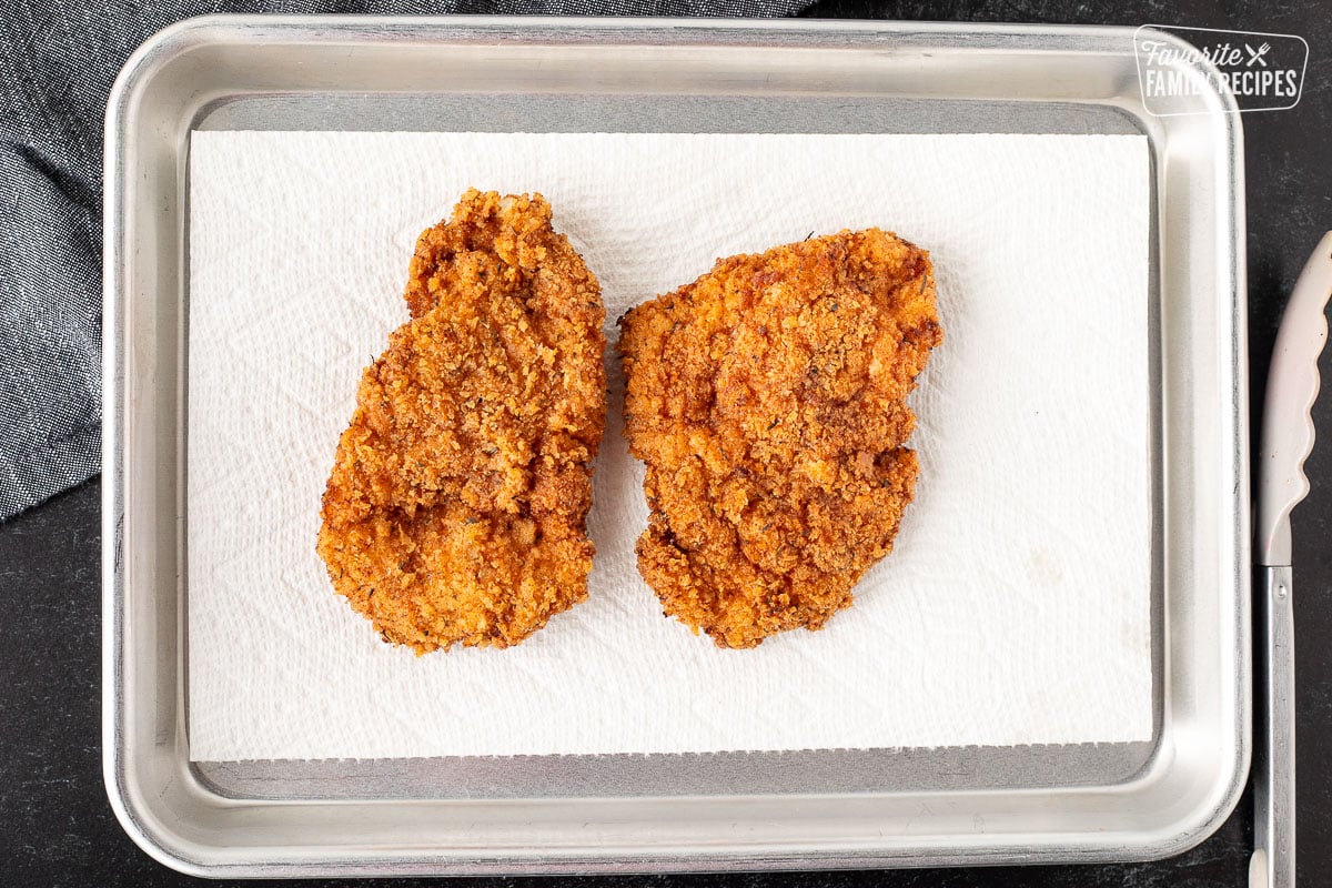 Two Fried chicken breasts on a pan lined with a paper towel.