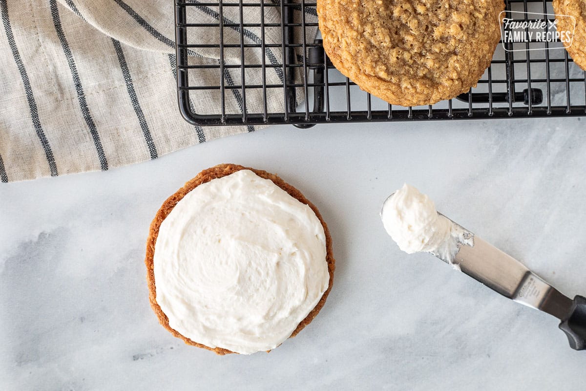 Spread marshmallow cream frosting on top of an oatmeal cookie.
