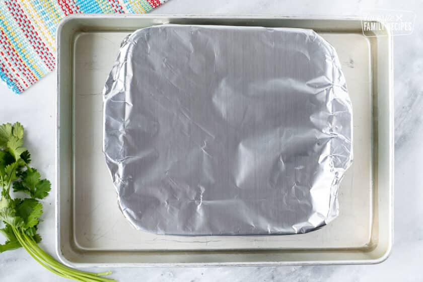 Casserole dish covered in foil in a baking pan of water.