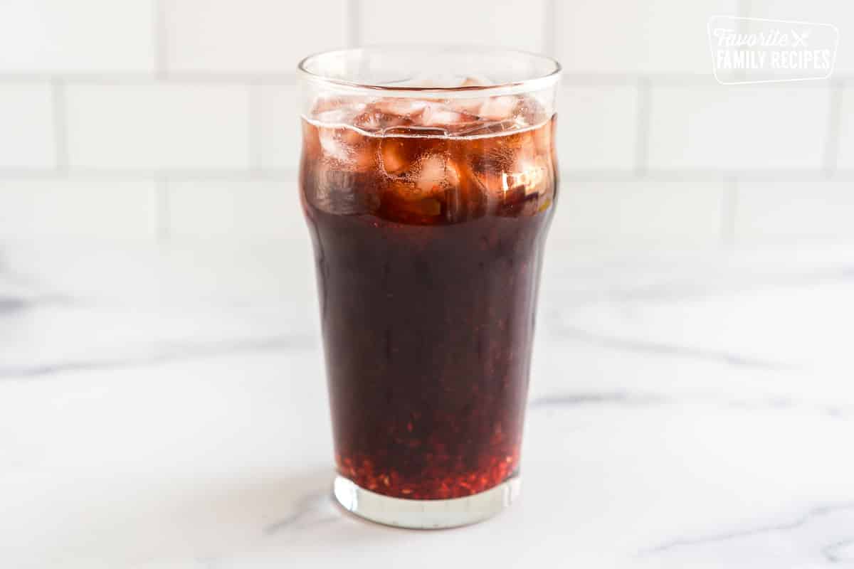 A glass with Dr. Pepper, ice, and raspberry puree